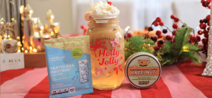 Photograph of items on table from left to right: Tasteless Protein Collagen sachet, Coconut Hazelnut Cloud Proffee in tall glass reading 'Holly Jolly', Flavoured Instant Coffee by Feel Good Coffee (Hazelnut) in a tin