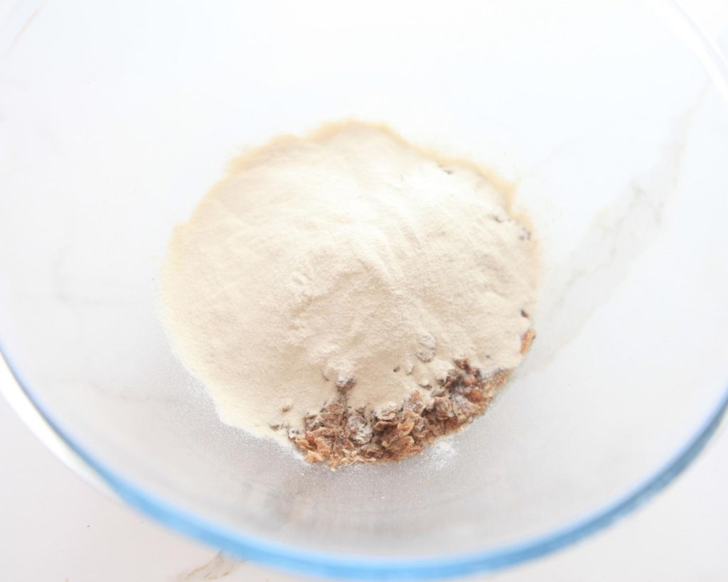 Meal replacement shake powder on top of crumbled Weet‑Bix sitting in a clear glass mixing bowl, photographed from above