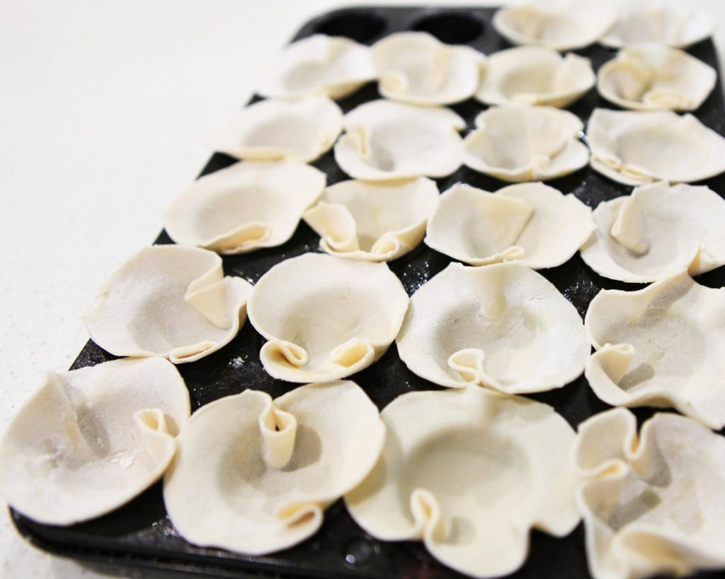 Uncooked dumpling wrappers placed in a mini muffin tin on a benchtop.