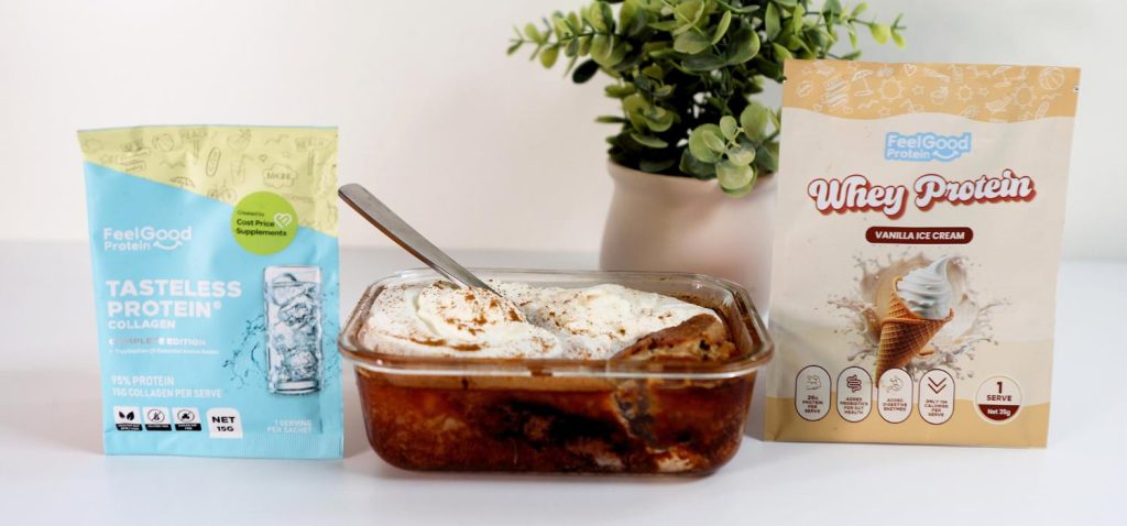 A yellow and blue Tasteless Protein Collagen sample sachet beside a clear baking dish filled with hot cross bun custard pudding topped with whipped cream, with a yellow Vanilla Ice Cream Whey Protein sachet on the other side, all placed on a white benchtop with a blurred plant in the background.