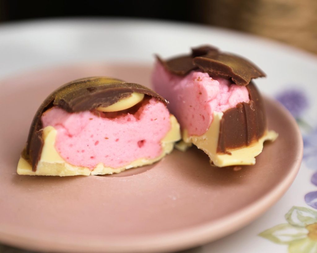 Shot of a Marshmallow Easter Egg cut in two on a pink plate, showing the brown, pink, and white layers inside.