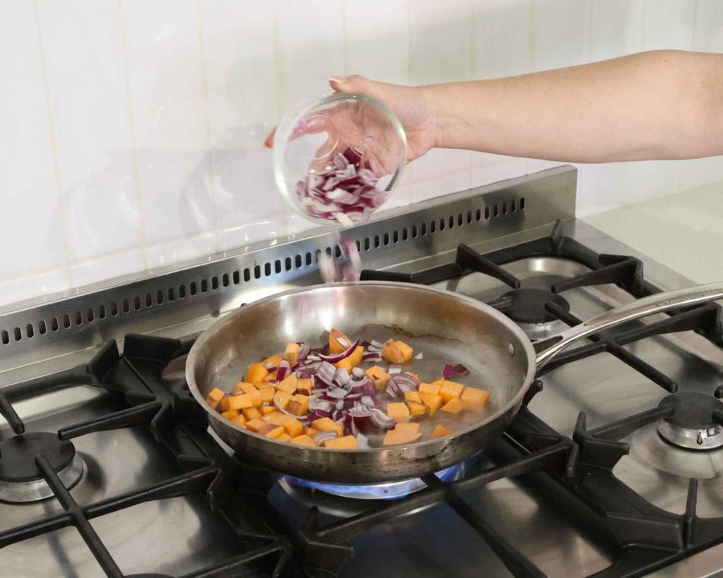 An image of the sliced red onion being added to the pan for the BBQ Chicken & Sweet Potato Muffins recipe