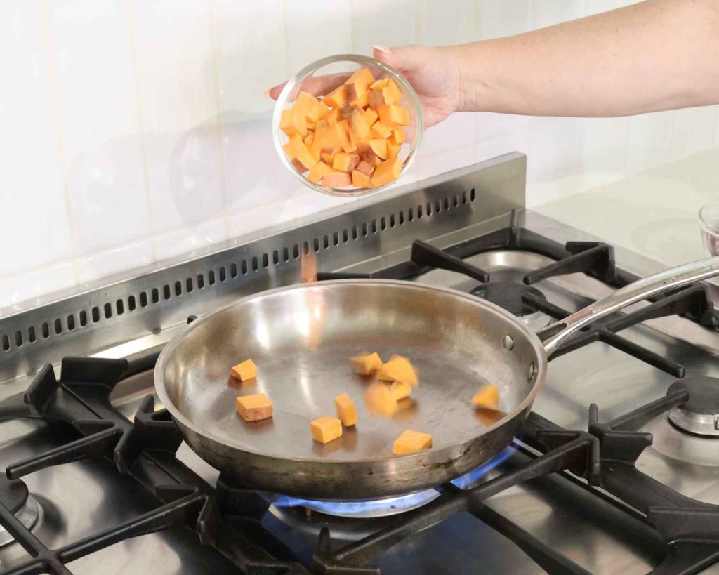 Diced sweet potato is being added to the heated pan for the BBQ Chicken & Sweet Potato Muffins recipe
