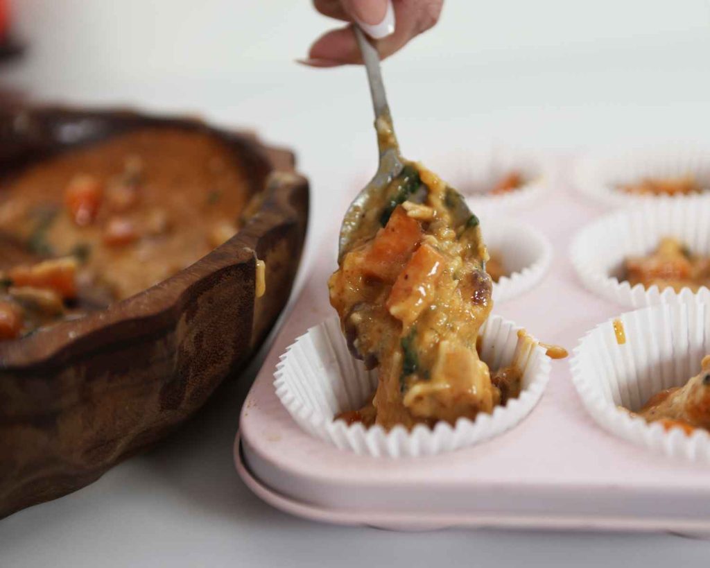 The BBQ Chicken & Sweet Potato Muffins recipe mixture is being added to the muffin tin