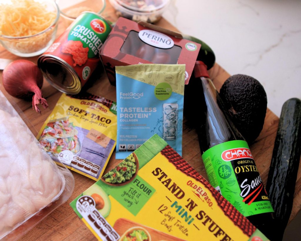 Overhead shot of Salsa Chicken Taco Boat ingredients spread out side by side on a wooden bench resting on a white benchtop. 