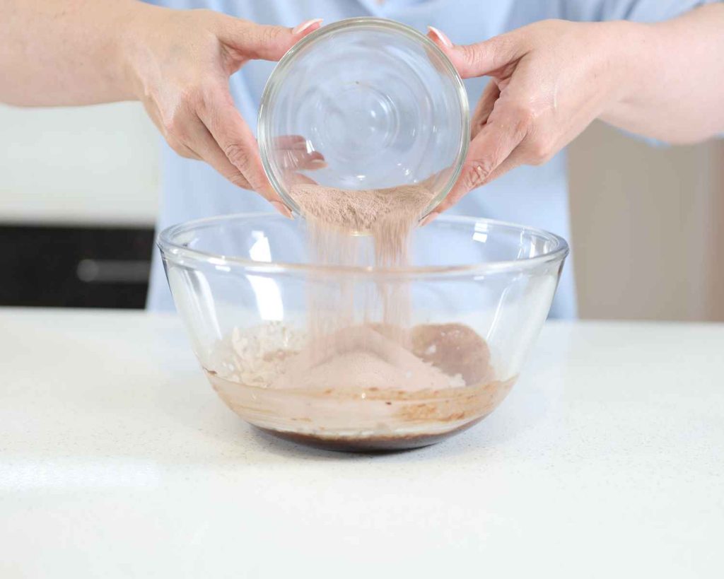 Adding whey protein by feel good protein to the bowl for the Chocolate Protein Easter Nests recipe