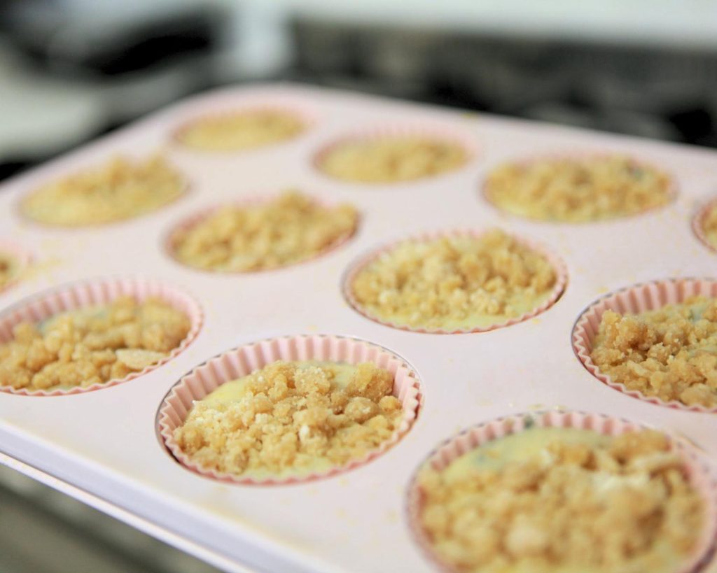 Pink muffin tray filled with blueberry muffins batter topped with crumble topping.