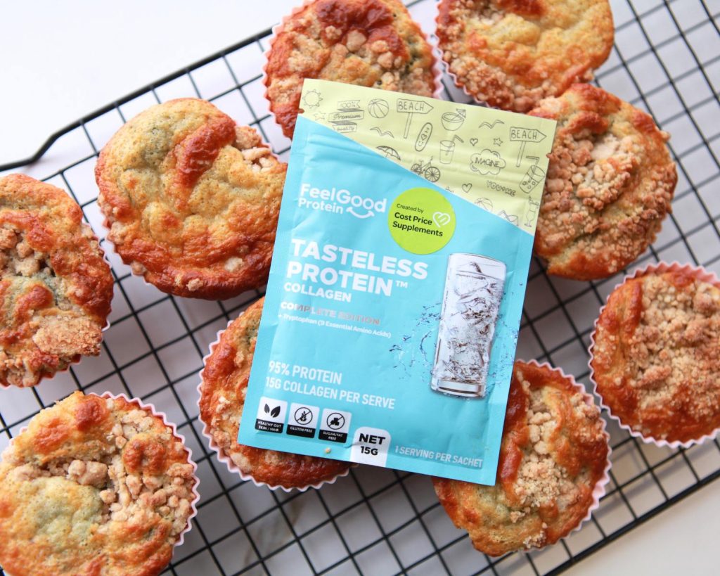 Top‑down view of a Feel Good Protein Tasteless Protein Collagen sachet in blue and yellow packaging centred on a black wire cooling rack with muffins around it. 