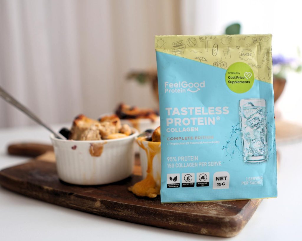 Front on photo of a yellow, blue, and white Tasteless Protein Collagan by Feel Good Protein sample sachet beside a ramekin filled with Blueberry French Toast, placed on across a wooden board in front of a blurred benchtop background. 