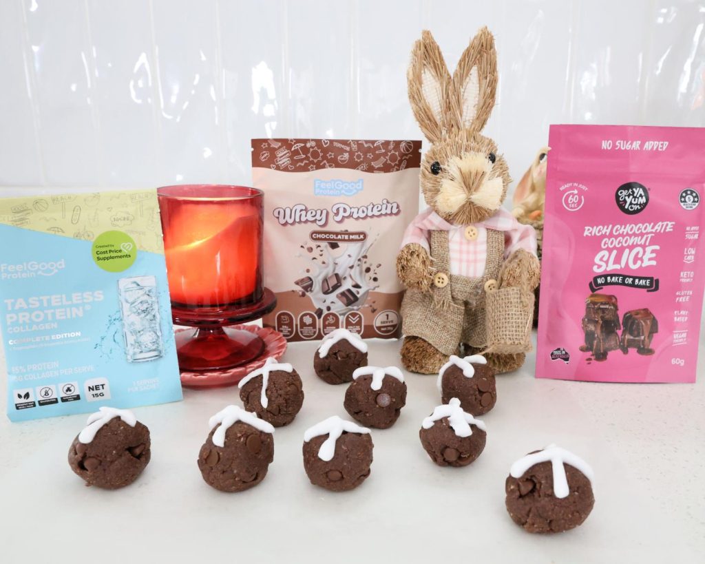 Front on photo of a Tasteless Protein Collagen by Feel Good Protein sachet, Whey Protein by Feel Good Protein (Chocolate Milk) sachet, and a Rich Chocolate Coconut Slice Mix by Get Ya Yum On sachet on both sides of a Easter bunny statue centred behind 9 protein balls.