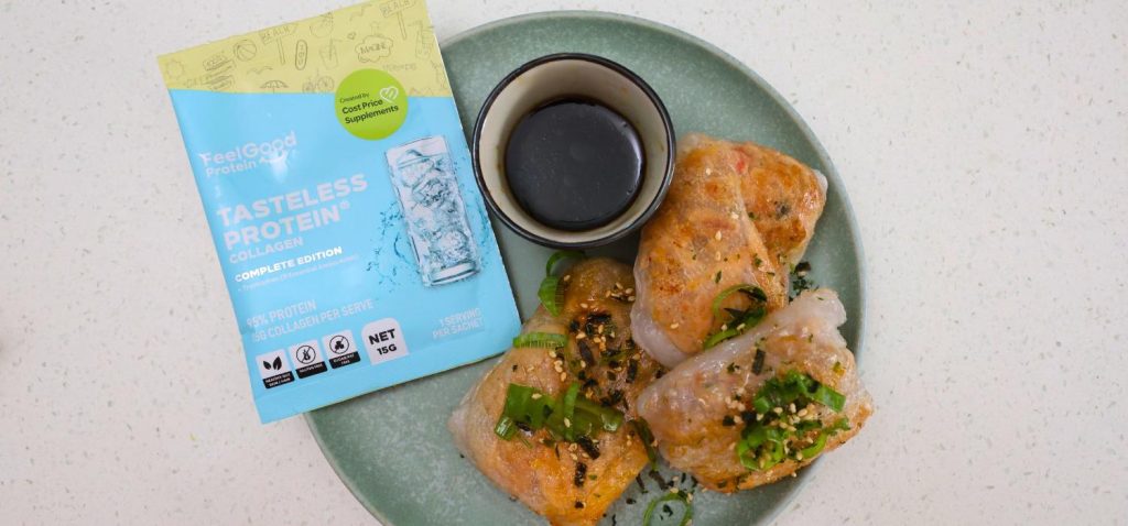 Top-down photo of a blue and yellow Tasteless Protein Collagen by Feel Good Protein sachet centred to the left on a plate next to a small white bowl with dipping sauce and 3 crispy rice paper parcels on a green plate.