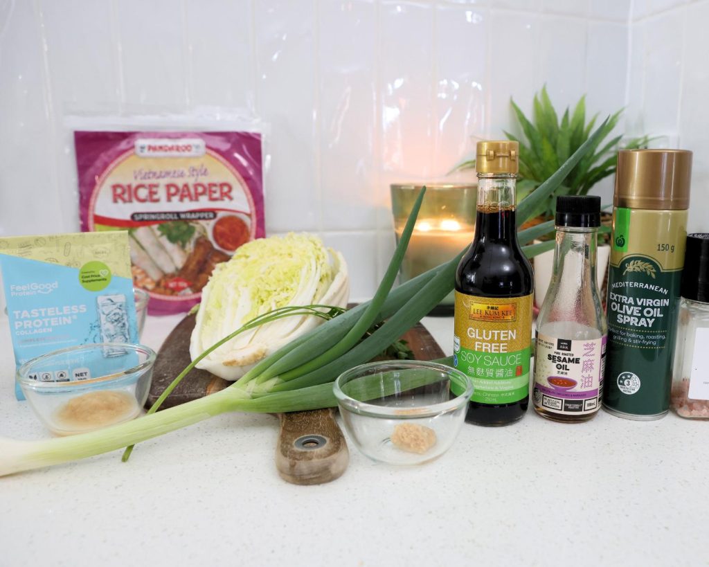 Front-facing photo showing all the ingredients for crispy rice paper parcels arranged side by side on a benchtop, with a softly blurred modern kitchen in the background.