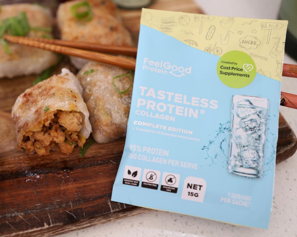 Front on photo of a yellow, blue, and white Tasteless Protein Collagen by Feel Good Protein sample sachet in front of 4 crispy rice paper parcels and a set of chopsticks, placed on across a wooden board in front of a blurred benchtop background.