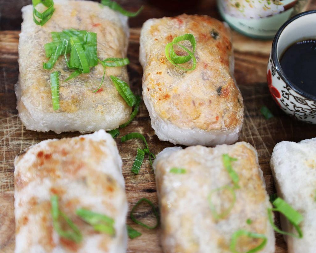 Overhead photo of 4 crispy rice paper parcels next to a small colourful dipping bowl filled with sauce, placed on across a wooden board.