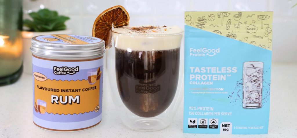 Front-facing photo of a metal cannister with orange and purple branding reading ‘Flavoured Instant Coffee Rum’, a Mont Blanc Proffee in a glass coffee cup, and a blue and yellow sachet of Tasteless Protein Collagen side by side, with a softly blurred modern kitchen in the background.