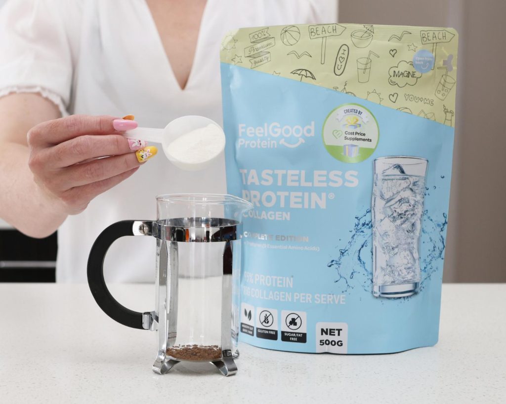Front-facing photo of a hand pouring a scoop of protein powder into a glass coffee press next to a bag of Tasteless Protein Collagen by Feel Good Protein. 