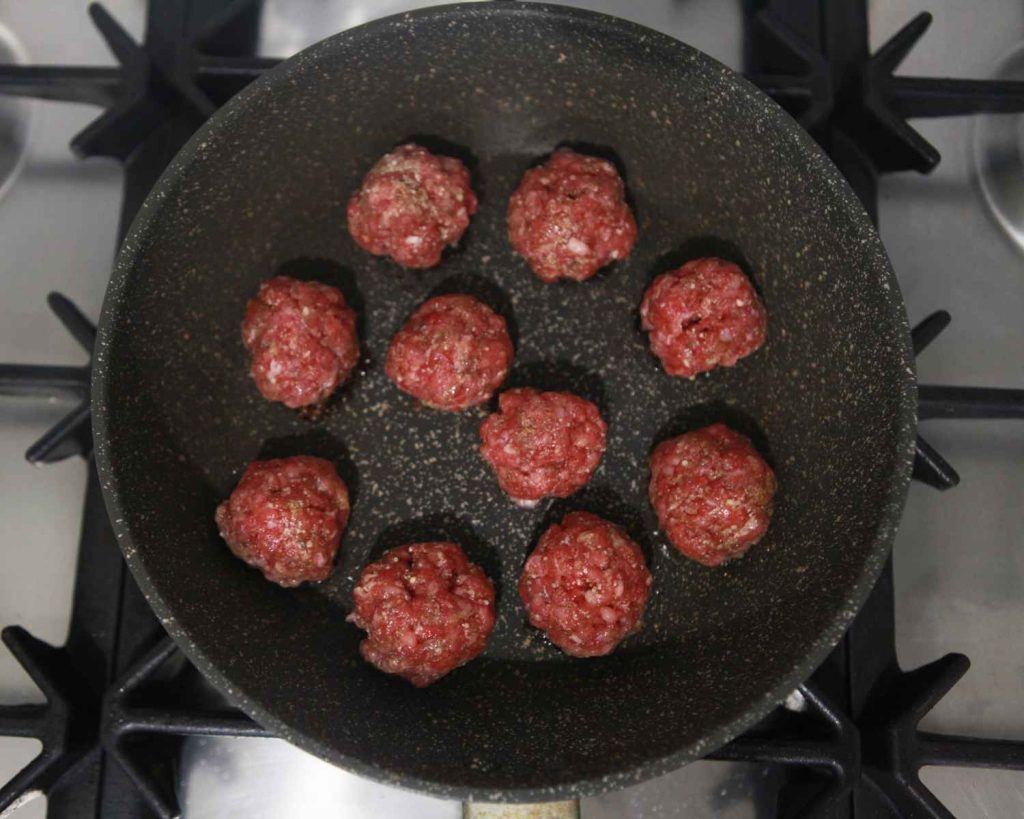 Raw meatballs being cooked in a pan
