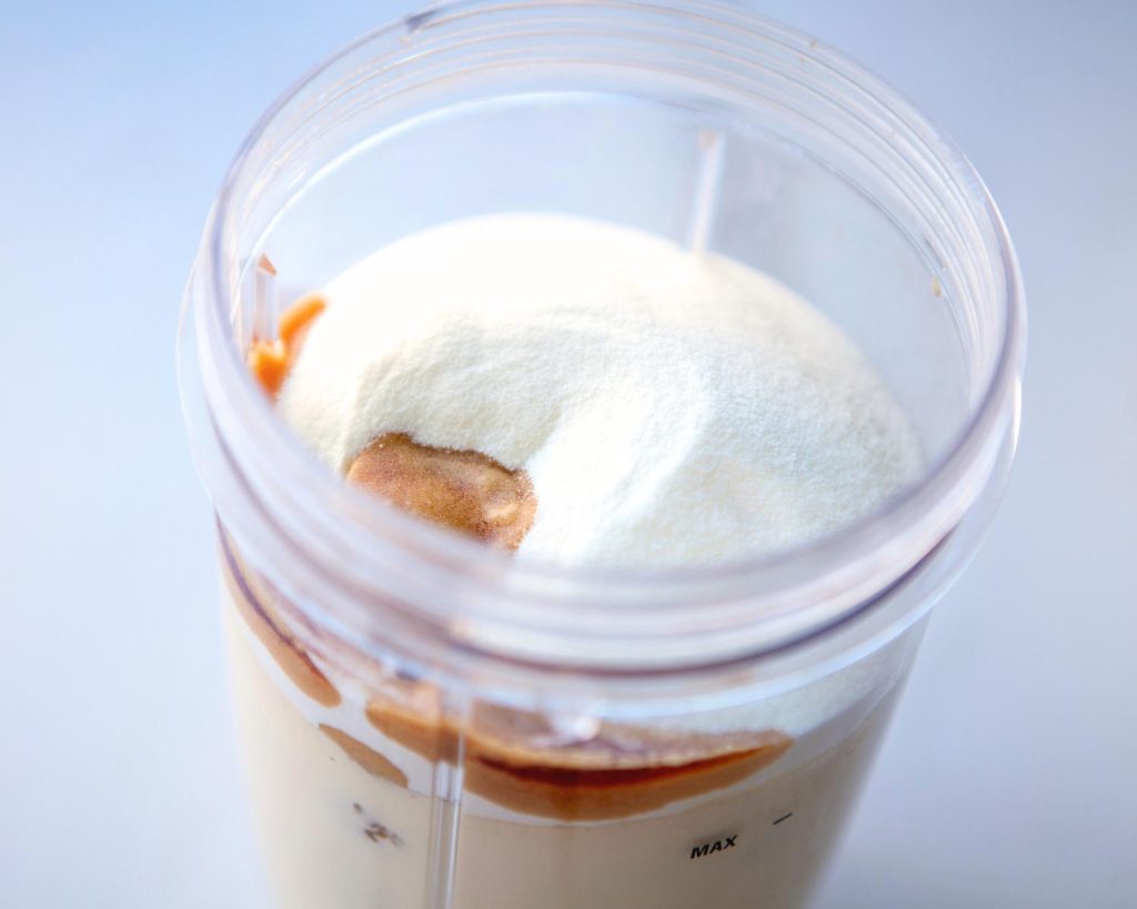 Top-down photo of a clear blender half filled with all the ingredients for Raspberry Swirl Protein Ice Cream with a softly blurred modern kitchen in the background. 
