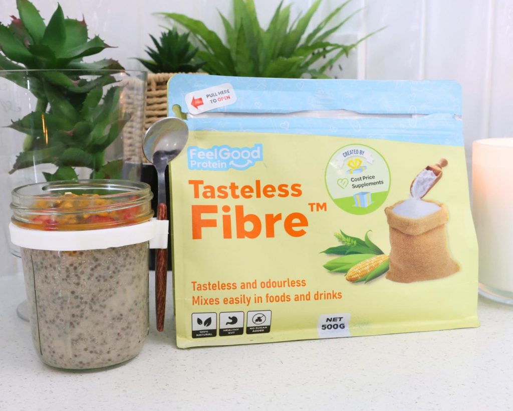 Front-facing photo of a glass container of High Protein Vanilla Ice Cream Chia Pudding next to a blue and yellow sachet of Tasteless Fibre by Feel Good Protein with a softly blurred modern kitchen in the background. 