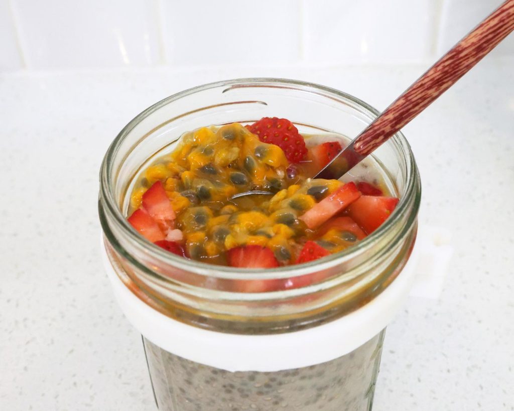 Top down photo of a glass container of High Protein Vanilla Ice Cream Chia Pudding topped with strawberries and passionfruit. 