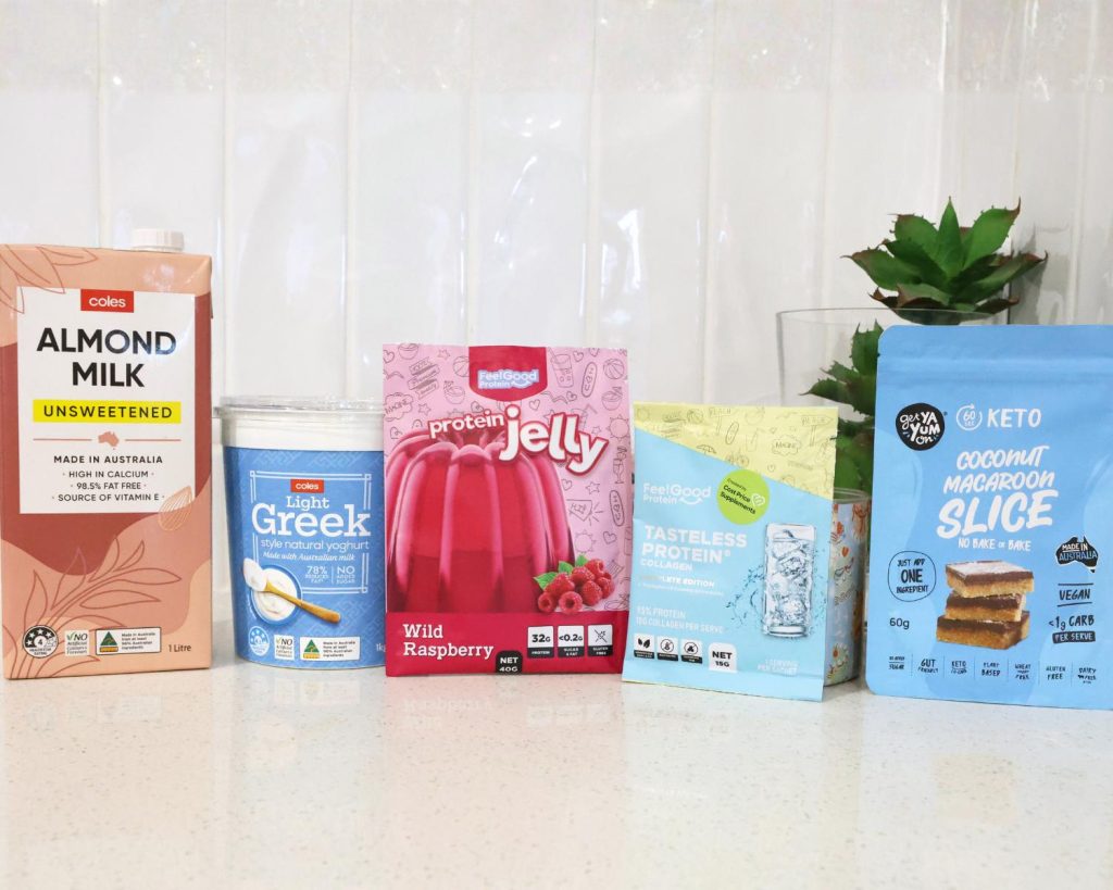 Front-facing photo showing all the ingredients for High Protein Raspberry Cheesecake Slice side by side on a benchtop, with a softly blurred modern kitchen in the background. 
