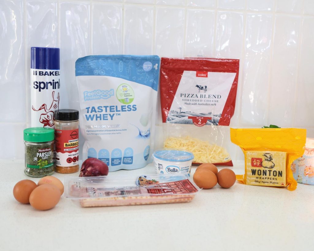 Front-facing photo showing all the ingredients for Bacon & Onion Protein Bites side by side on a benchtop, with a softly blurred modern kitchen in the background. 