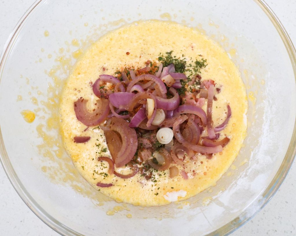 Birds eye view photo of a glass mixing bowl filled the Bacon & Onion Protein Bites mixture with a softly blurred modern kitchen in the background. 