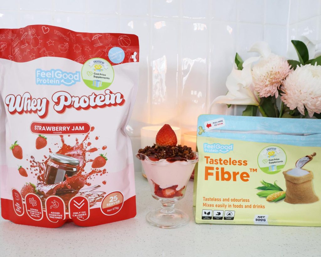 Front on photo of a red and pink back of Whey Protein by Feel Good Protein (Strawberry Jam) on the left of a Strawberry Cheesecake Protein Bowl, with a yellow and blue bag of Tasteless Fibre by Feel Good Protein on the right hand side. 