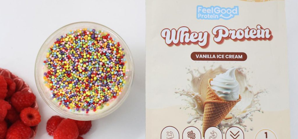 Front on photo of a yellow packet of Whey Protein by Feel Good Protein (Vanilla Ice Cream) on the right side of a glass bowl of High Protein Viral Dot Cake placed on a kitchen bench.
