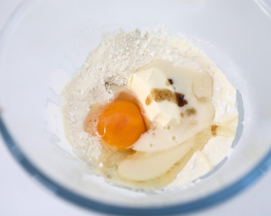 Birds eye view photo of a glass mixing bowl filled the High Protein Viral Dot Cake ingredients with a softly blurred modern kitchen in the background. 