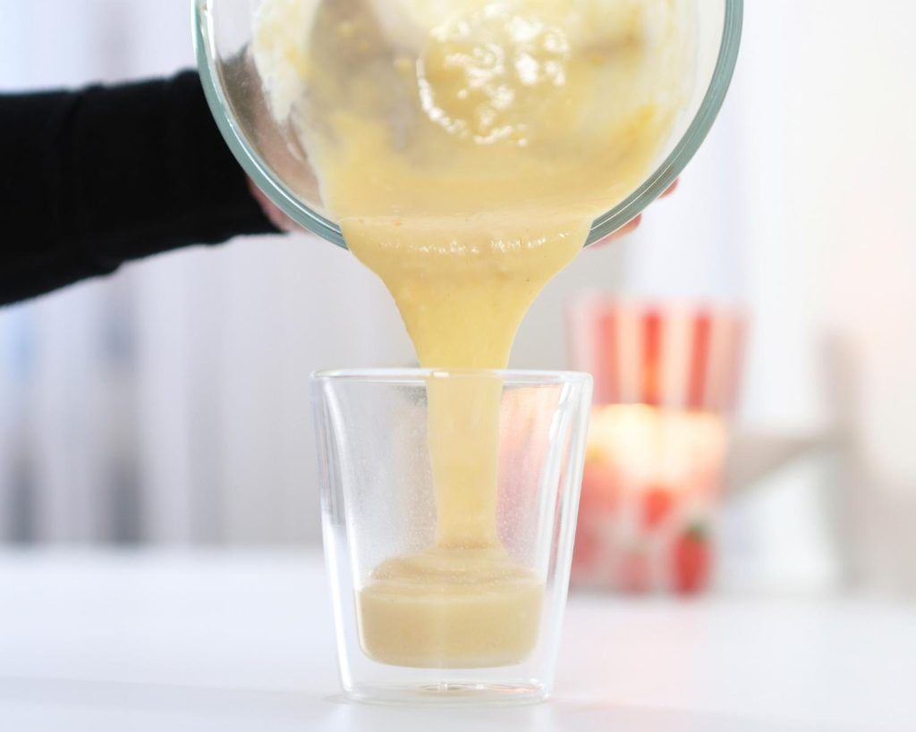 Front-facing photo of a hand pouring yellow cake batter into a glass bowl. 
