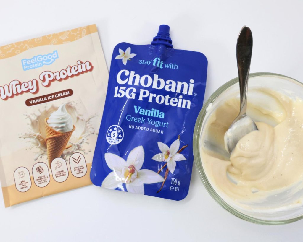 Birds eye view photo of a glass mixing bowl filled the High Protein Viral Dot Cake batter, next to a blue pouch of Chobani with a yellow packet of Whey Protein by Feel Good Protein (Vanilla Ice Cream) on the left side. 