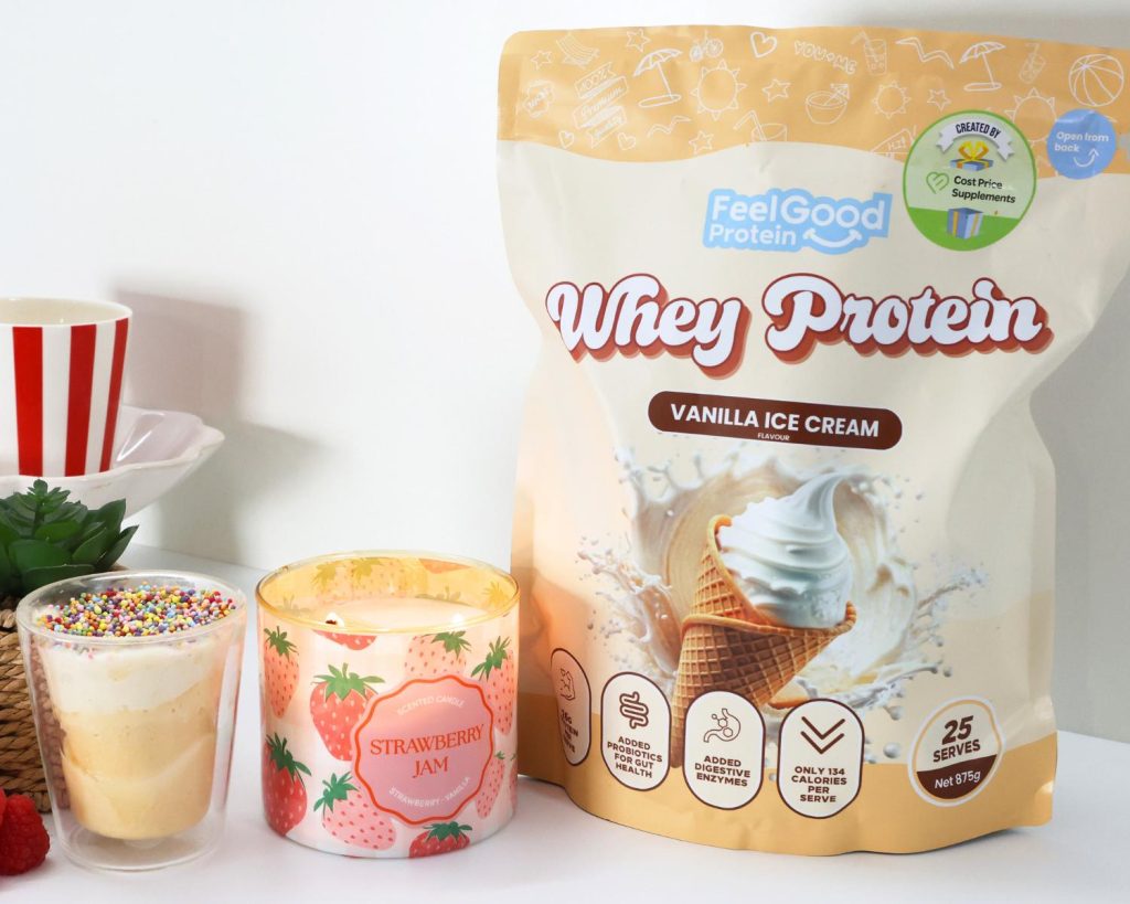 Front on photo of a yellow packet of Whey Protein by Feel Good Protein (Vanilla Ice Cream) on the left of a candle and a glass bowl of High Protein Viral Dot Cake. 